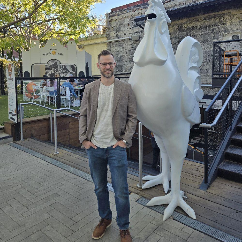 Wes standing in front of a giant white rooster by the Annaheim Packing House.